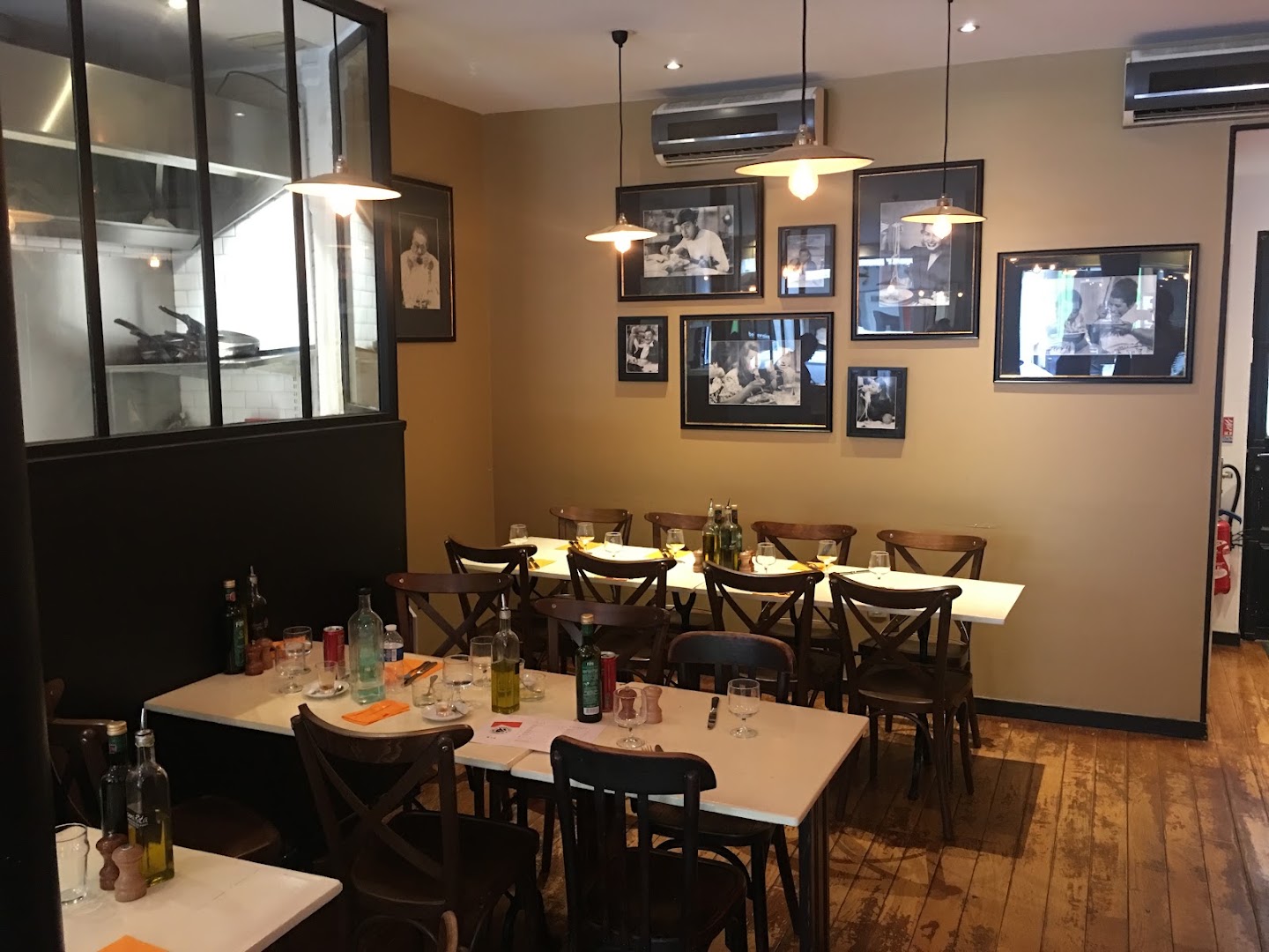 La salle de Bistrattoria Nonna Rita avec ses tables en bois et sa cuisine vitrée